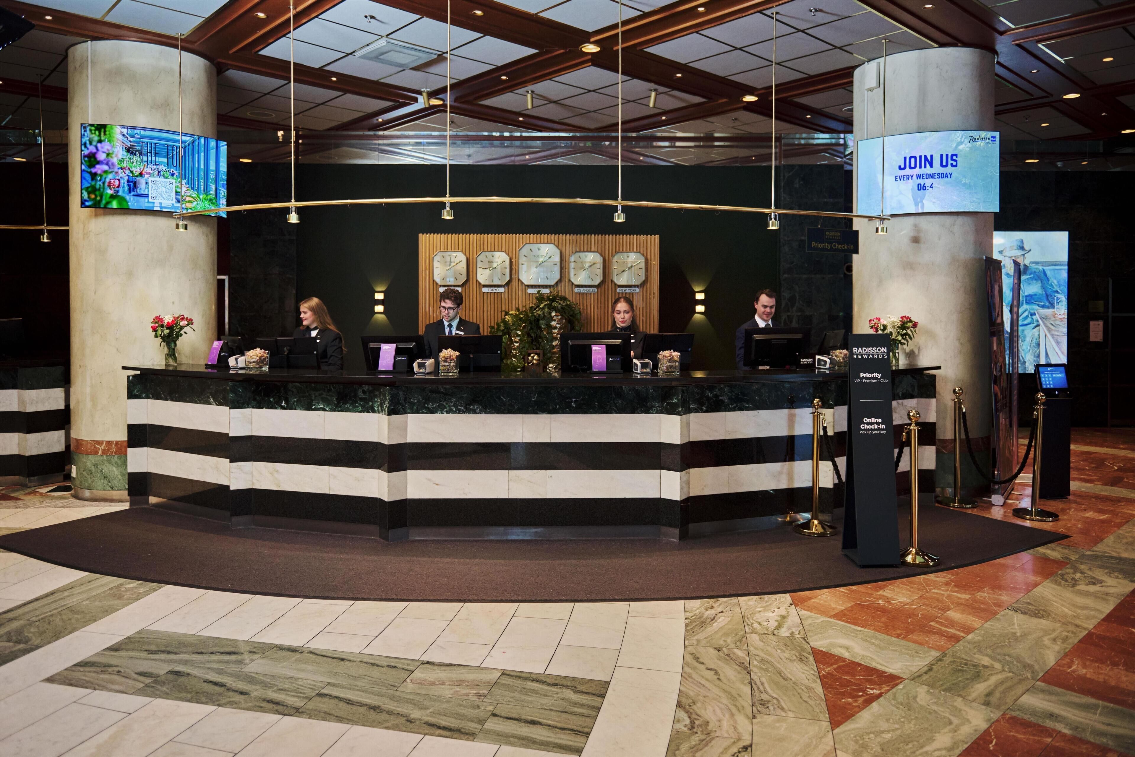 A reception desk with four staff members, a large digital screen, and a 'Join Us' sign.