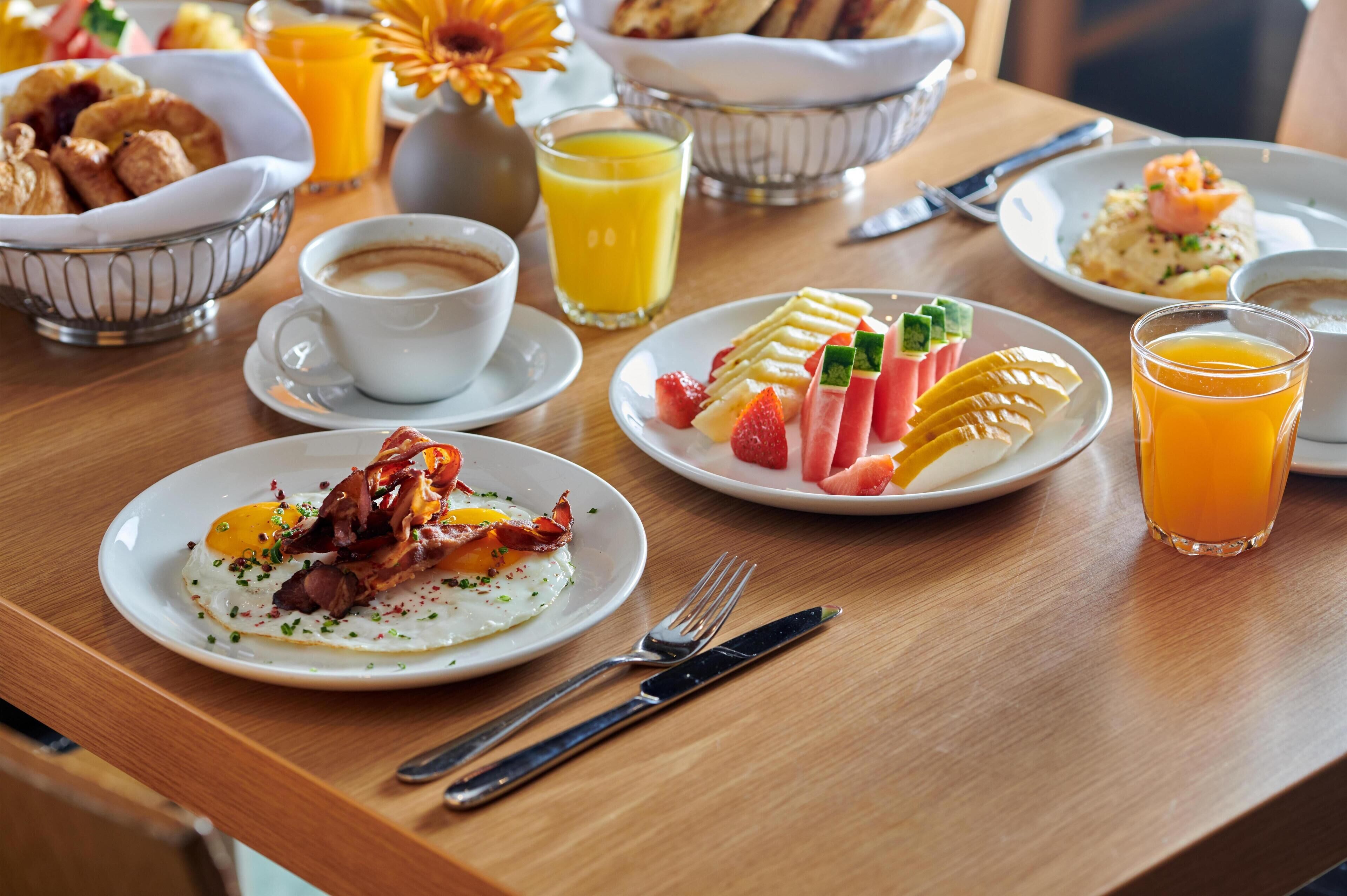 Et morgenbord med croissanter, æg, bacon, frugt og appelsinjuice.