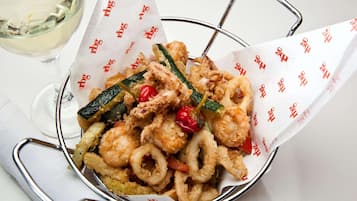 A basket of fried calamari with vegetables, accompanied by a glass of white wine.