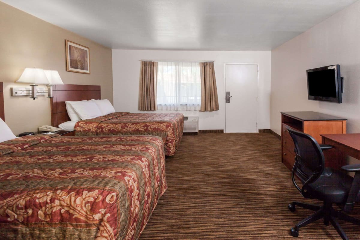A hotel room with two beds, a desk, a chair, a television, and a window with curtains.