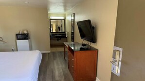 A hotel room with a bed, a wooden desk, a television, a microwave, and a bathroom visible in the background.