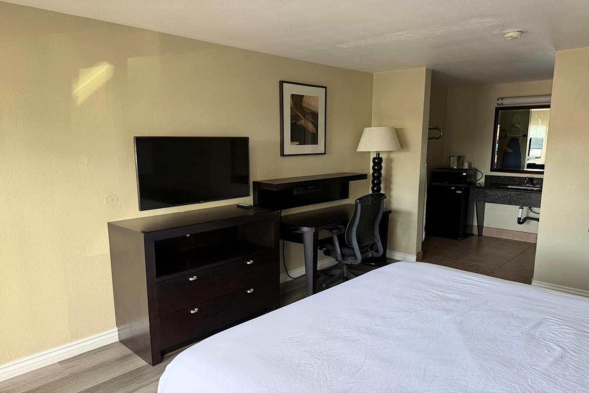 A hotel room with a bed, a desk, a chair, a television, a lamp, and a bathroom visible through an open door.
