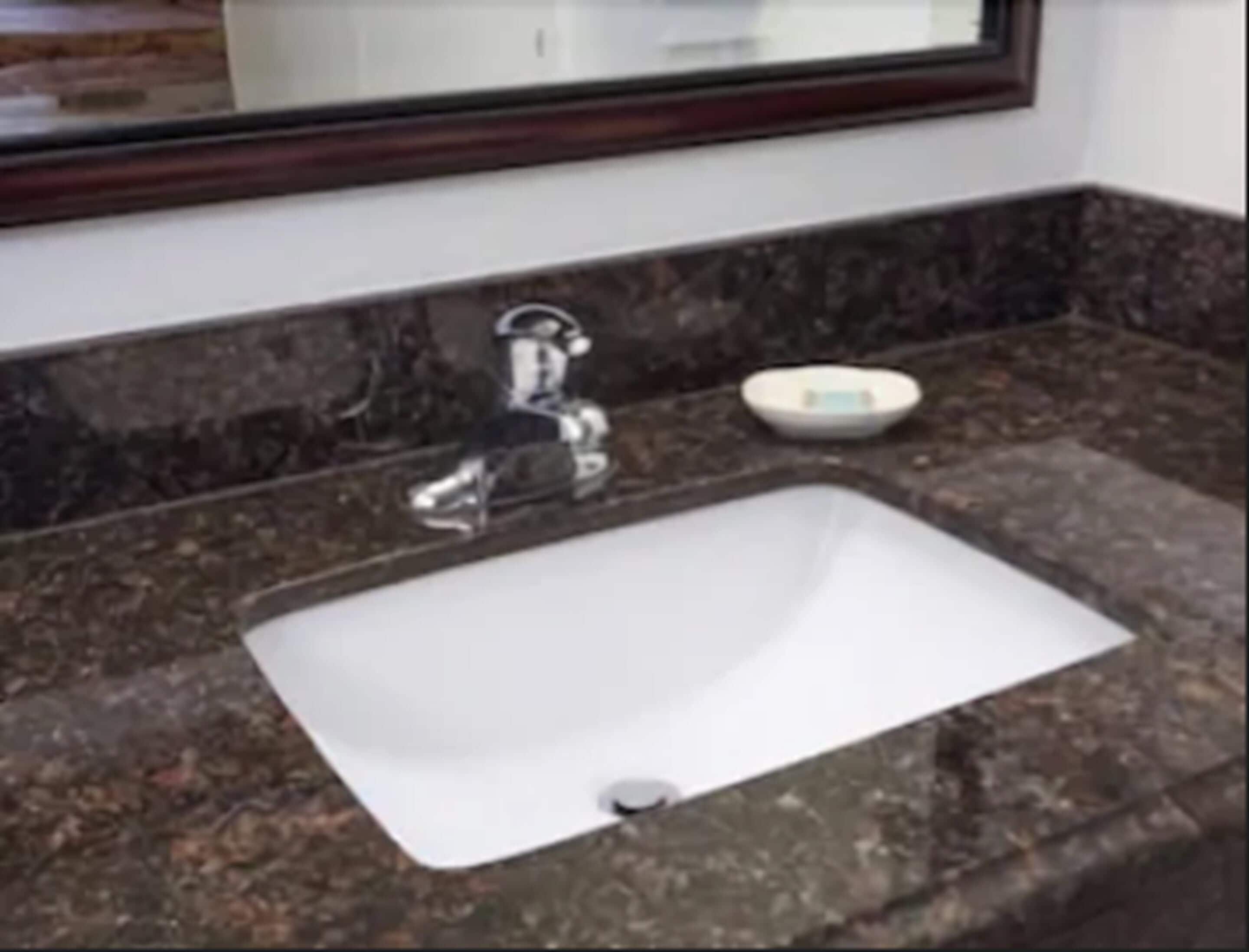 Une salle de bain avec un lavabo blanc, un miroir et un porte-savon, le tout posé sur un comptoir en granit.