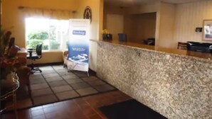 A hotel reception area with a marble counter, a chandelier, a reception desk, and a window with a view of greenery.