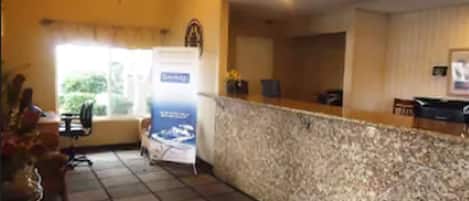 A hotel reception area with a marble counter, a chandelier, a reception desk, and a window with a view of greenery.