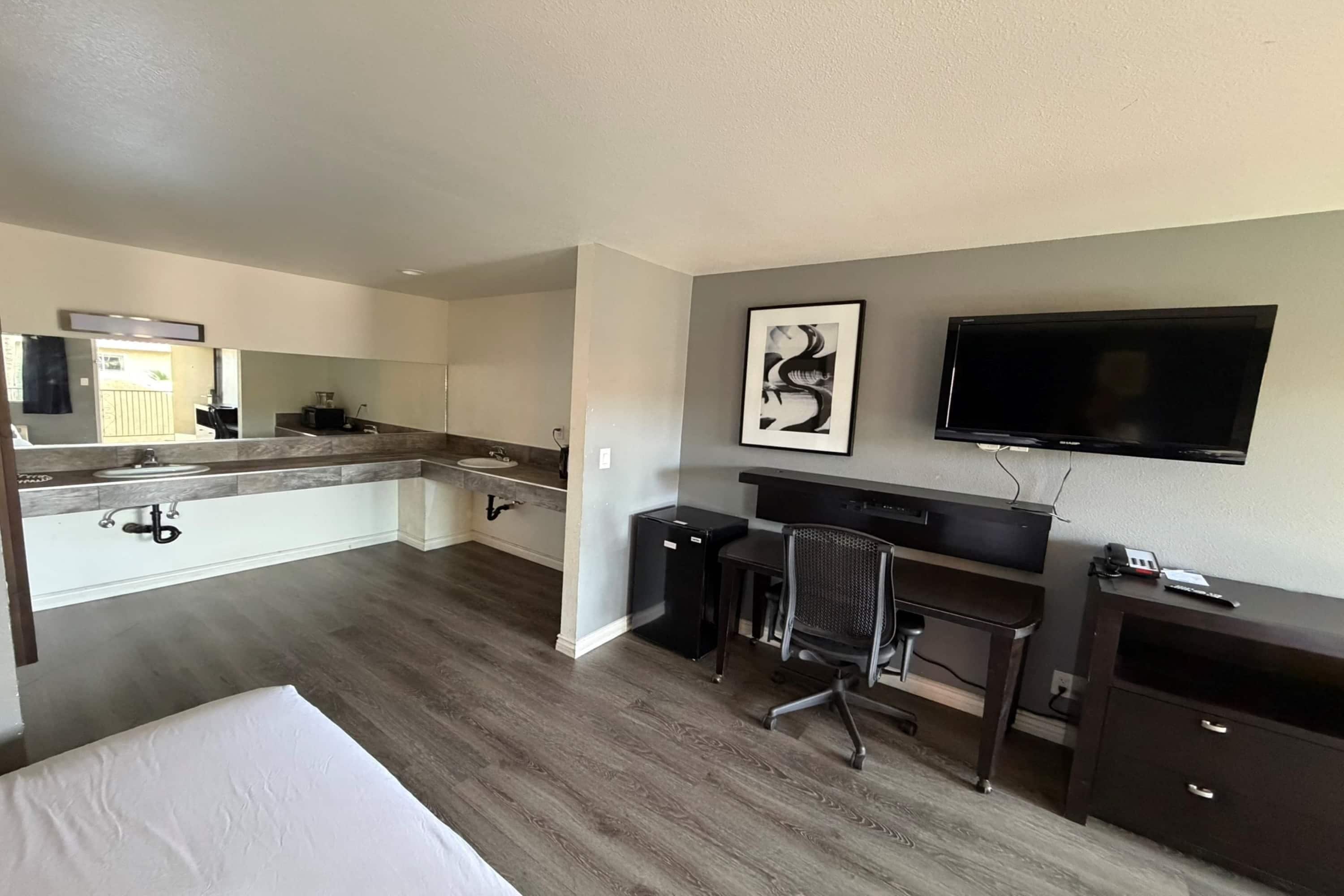 Hotelkamer met een bed, een bureau met stoel, een televisie, een schilderij en een kitchenette.