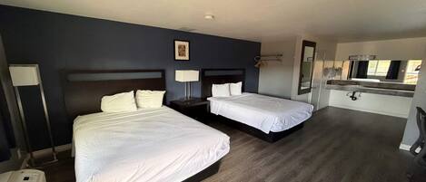 A hotel room with two beds, a small desk, a mirror, and a window.