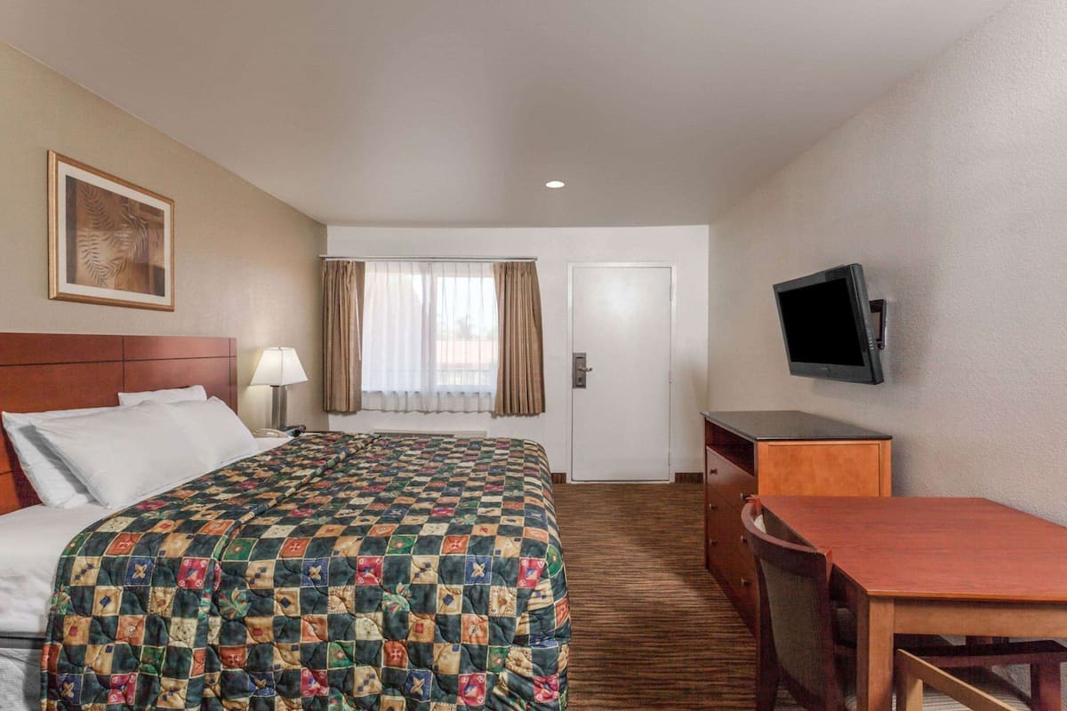 A hotel room with a bed, a desk, a television, a door, and a window with curtains.
