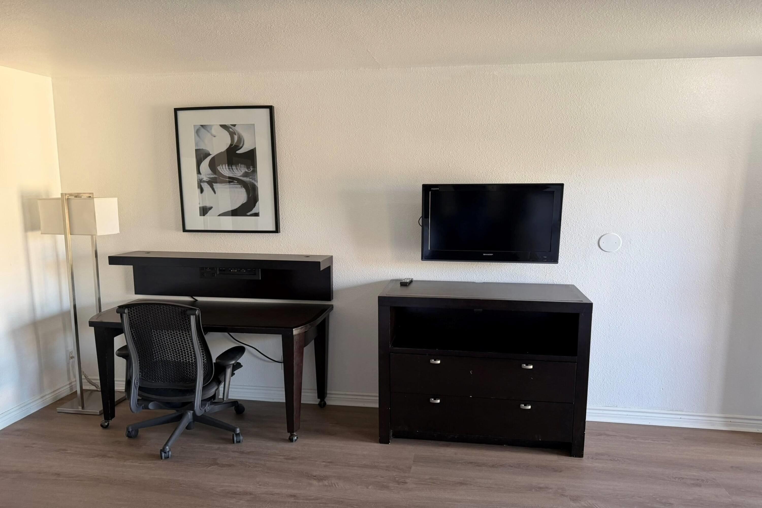 Una habitación con escritorio, silla, televisión y un armario pequeño.