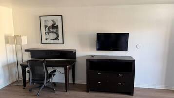 Una habitación con escritorio, silla, televisión y un armario pequeño.