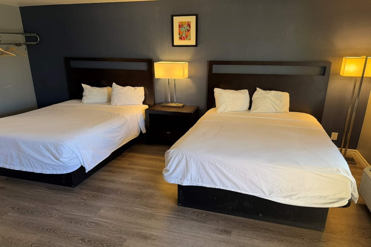 A hotel room with two beds, a nightstand with a lamp, a framed picture on the wall, and a hanging coat rack.