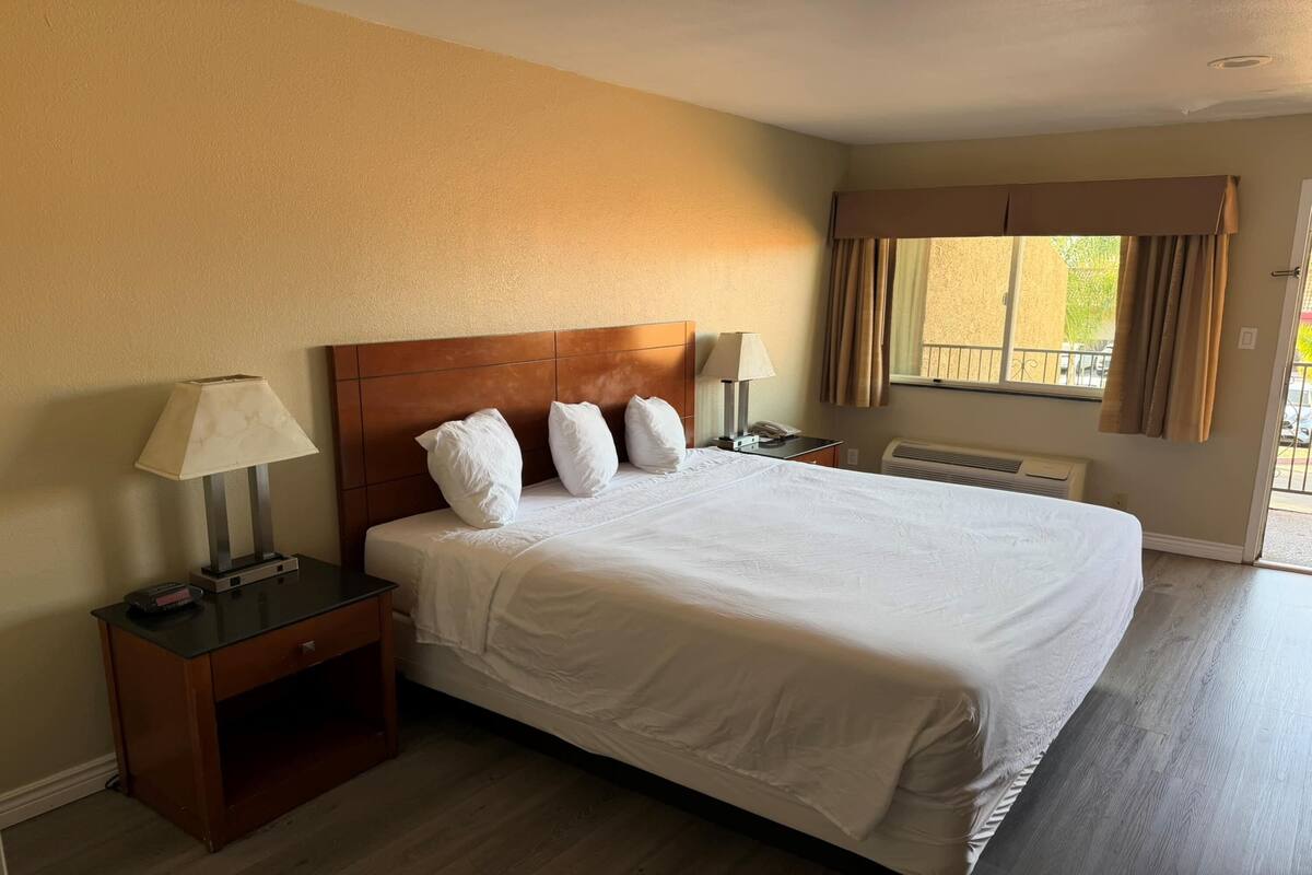 A hotel room with a large bed, two bedside tables, a nightstand, a window with curtains, and a view of the outside.