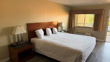 A hotel room with a large bed, two bedside tables, a nightstand, a window with curtains, and a view of the outside.