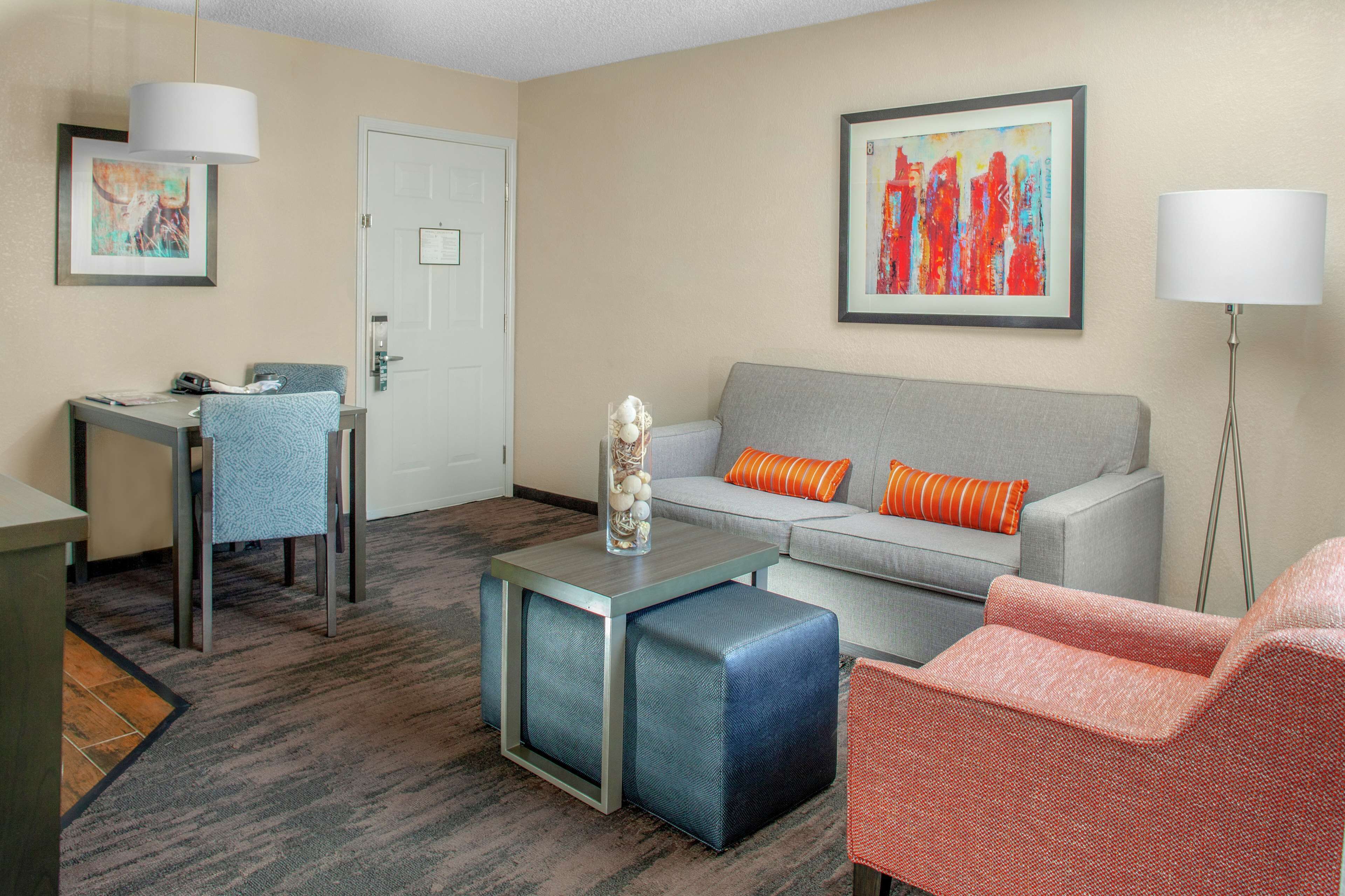 A hotel room with a gray sofa, a small table, a chair, and a floor lamp.