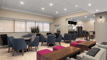 A modern lounge area with seating arrangements, a bar, and a television screen.