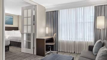 Ein Hotelzimmer mit einem Bett, einem Schreibtisch mit Stuhl, einem Sofa und einem großen Fenster mit Vorhängen.