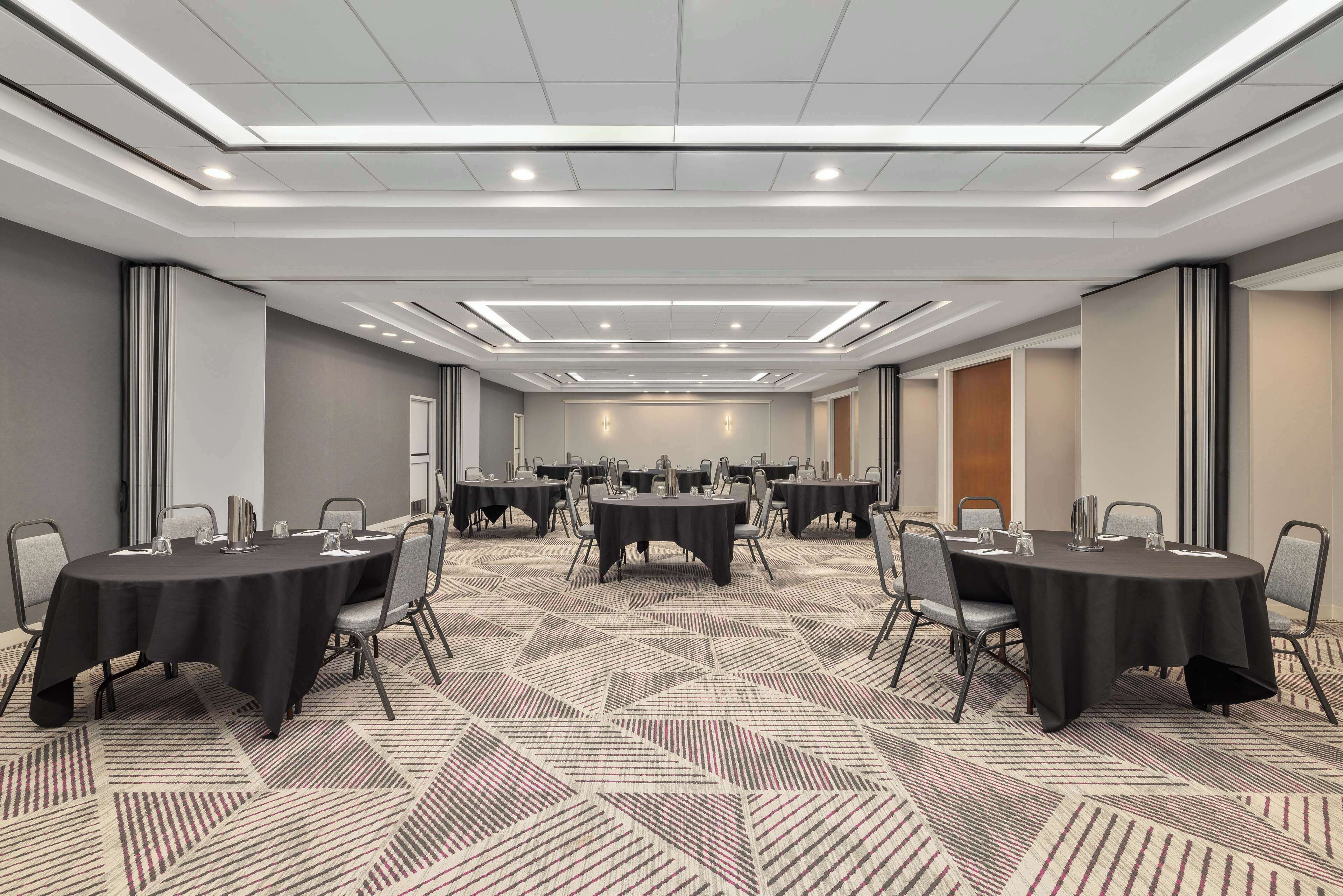 A conference room with multiple tables and chairs, a patterned carpet, and recessed lighting.