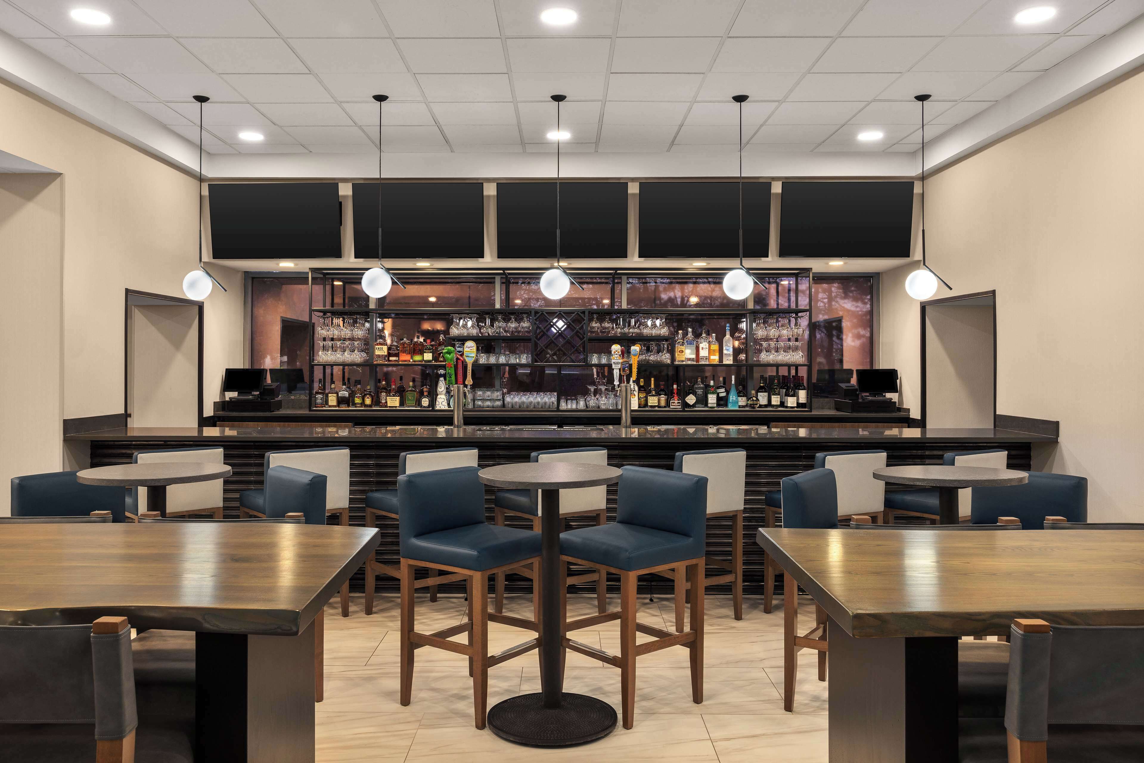A bar area with multiple seating options, including round tables and chairs, and a well-stocked bar counter with various bottles and glasses.