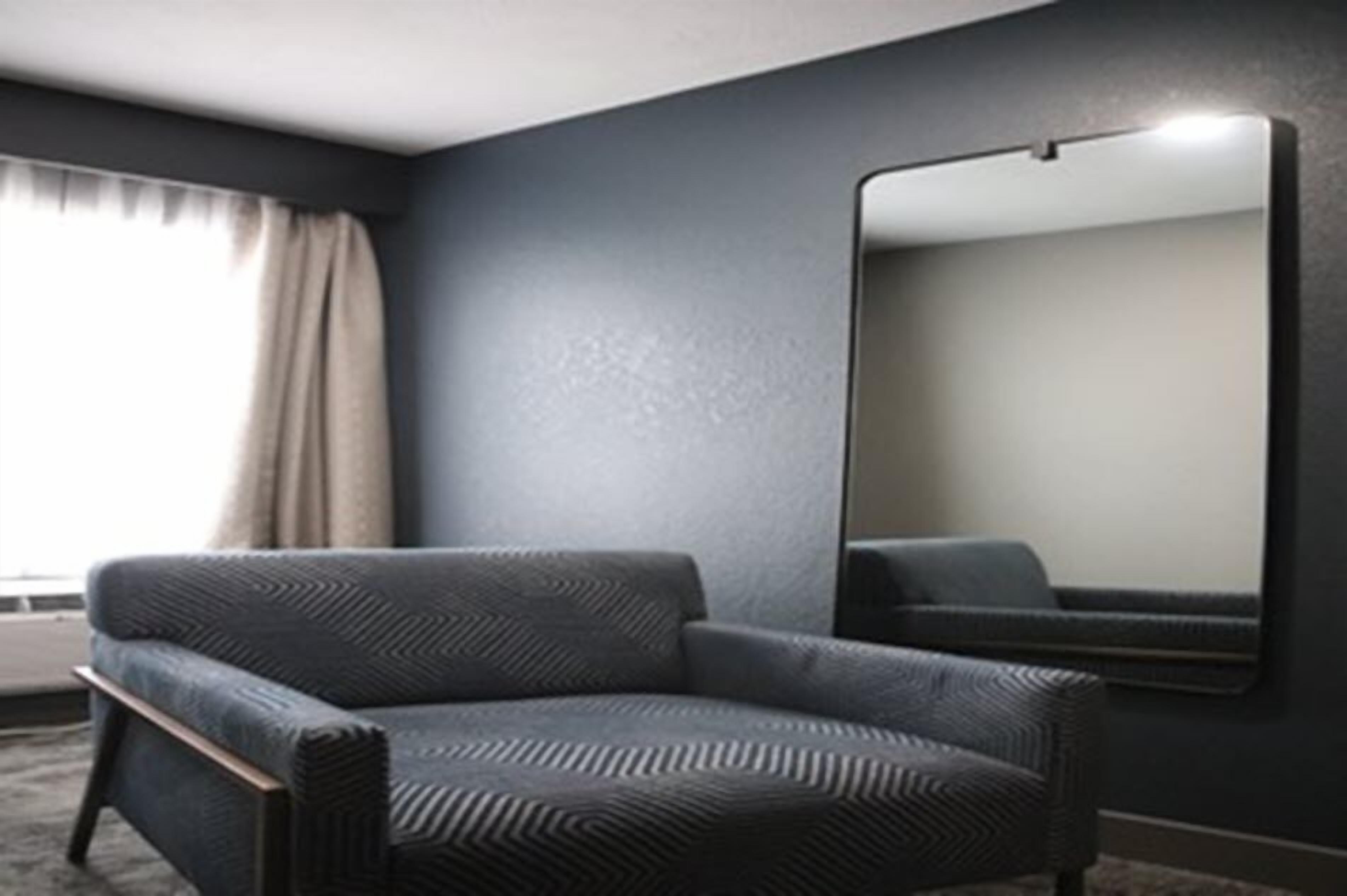 A modern room with a dark blue wall, a large mirror, and a dark blue armchair.