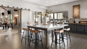 A modern kitchen with a central island, bar stools, and a view into the dining area. - Eastland Suites Hotel & Conference Ctr, Trademark by Wyndham (Bloomington)