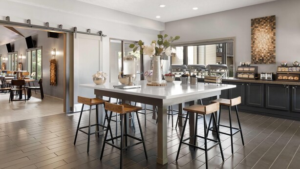 A modern kitchen with a central island, bar stools, and a view into the dining area.