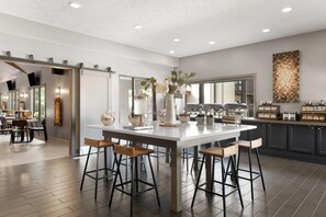 A modern kitchen with a central island, bar stools, and a view into the dining area. - Eastland Suites Hotel & Conference Ctr, Trademark by Wyndham (Bloomington)