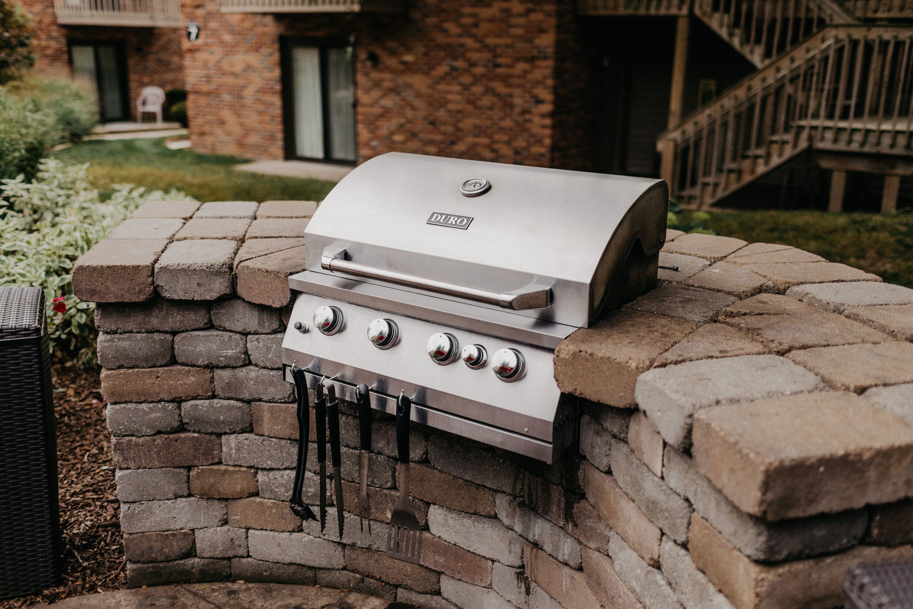 A Duro gas grill built into a brick wall, with a staircase and a building in the background.