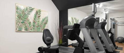 Et fitnessrum med løbebånd og træningsudstyr, et stort spejl og et maleri af palmeblade på væggen.