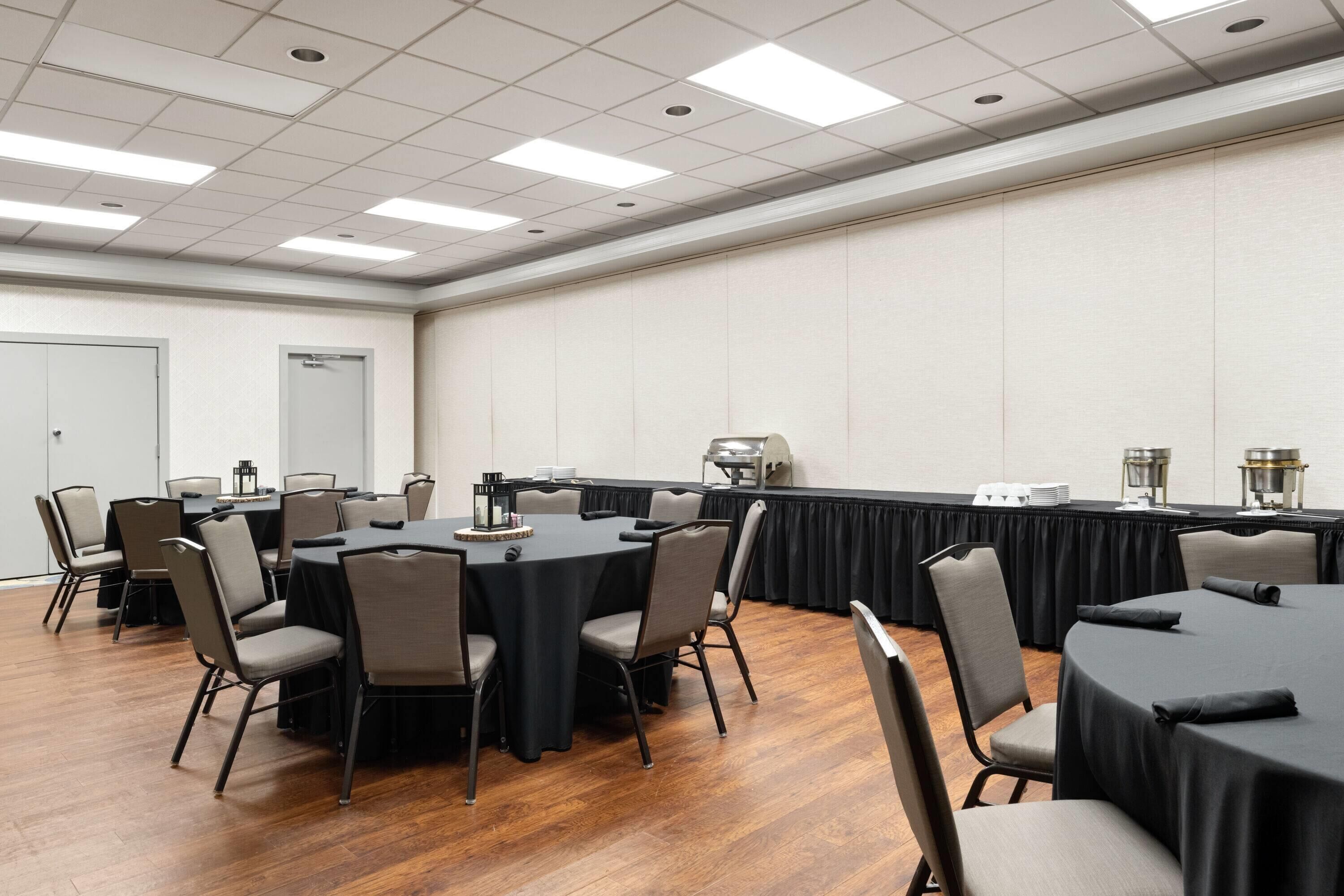 Une salle de conférence avec des tables rondes et des chaises, une nappe noire et un plancher en bois.