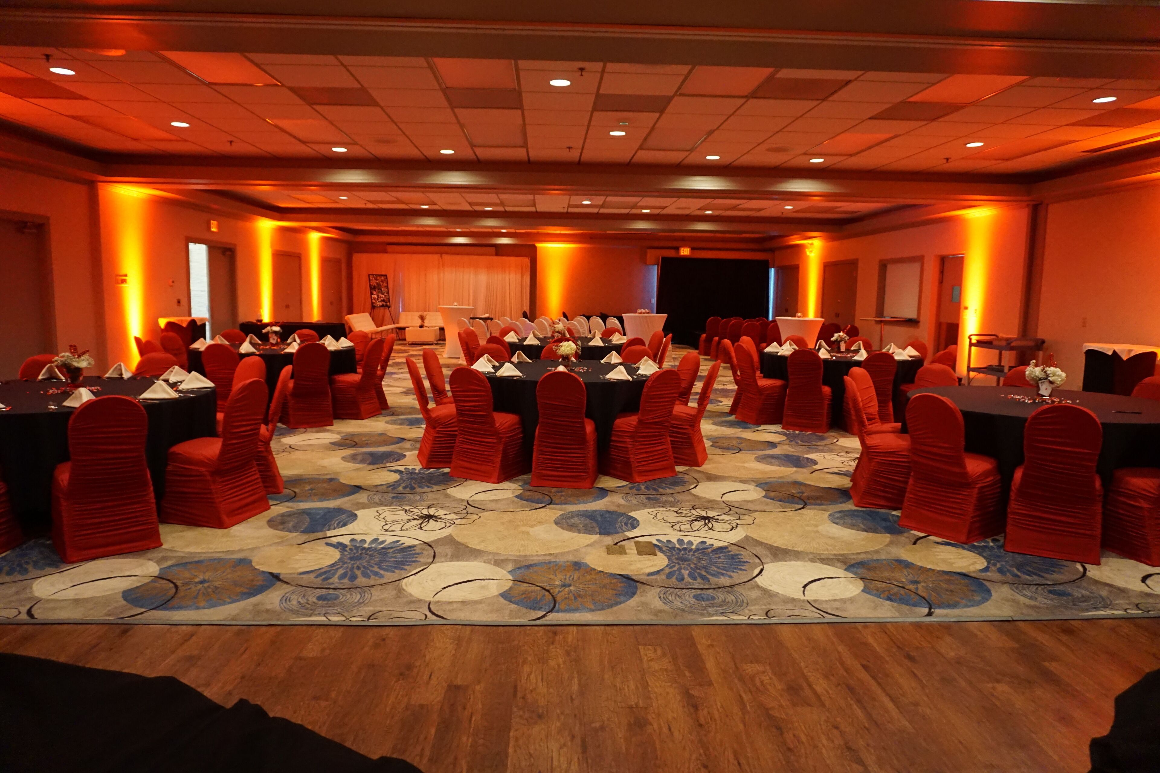 Un salón de conferencias con mesas redondas, sillas rojas y una alfombra estampada.