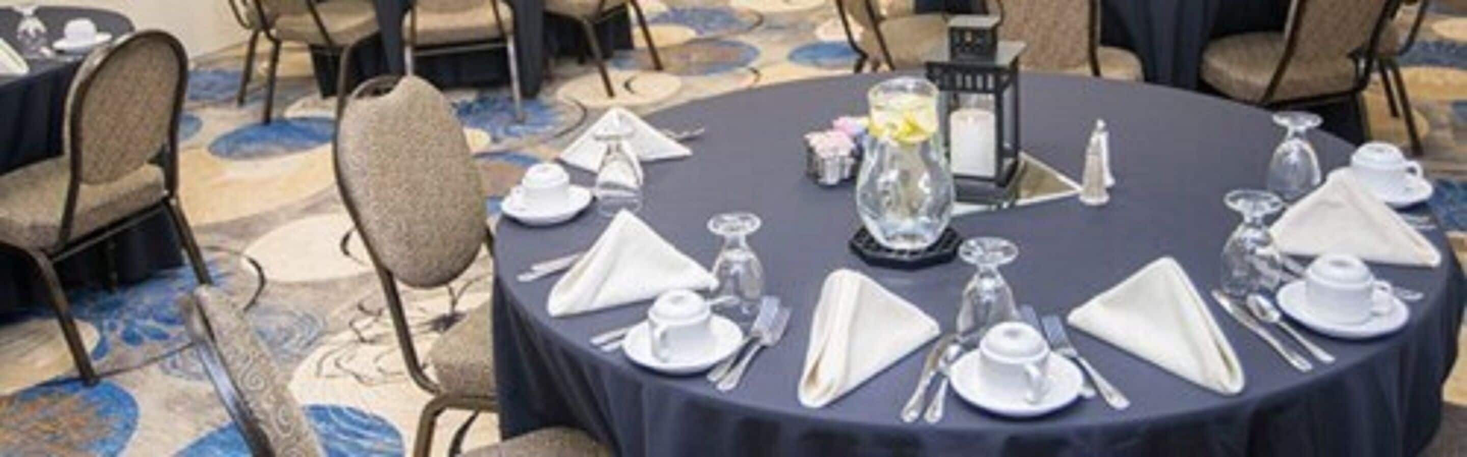 A round table set for a formal event with white tableware and a candle centerpiece.