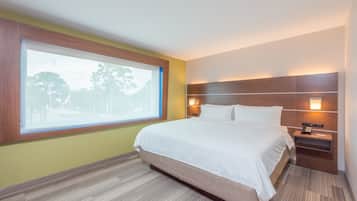 Habitación de hotel con un ventanal grande, una cama, una mesita de noche y un aplique de pared.