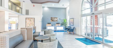 A hotel lobby with a reception desk, seating area, and large windows.