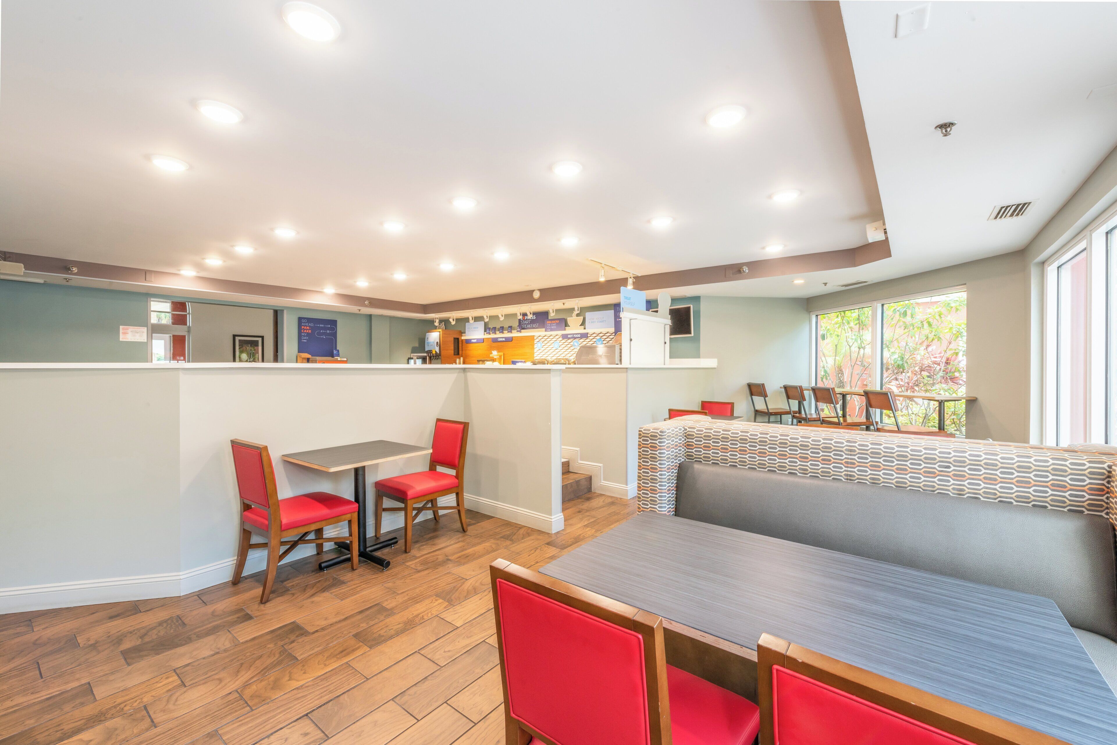 A modern restaurant with a bar area, seating arrangements, and a view of greenery outside.