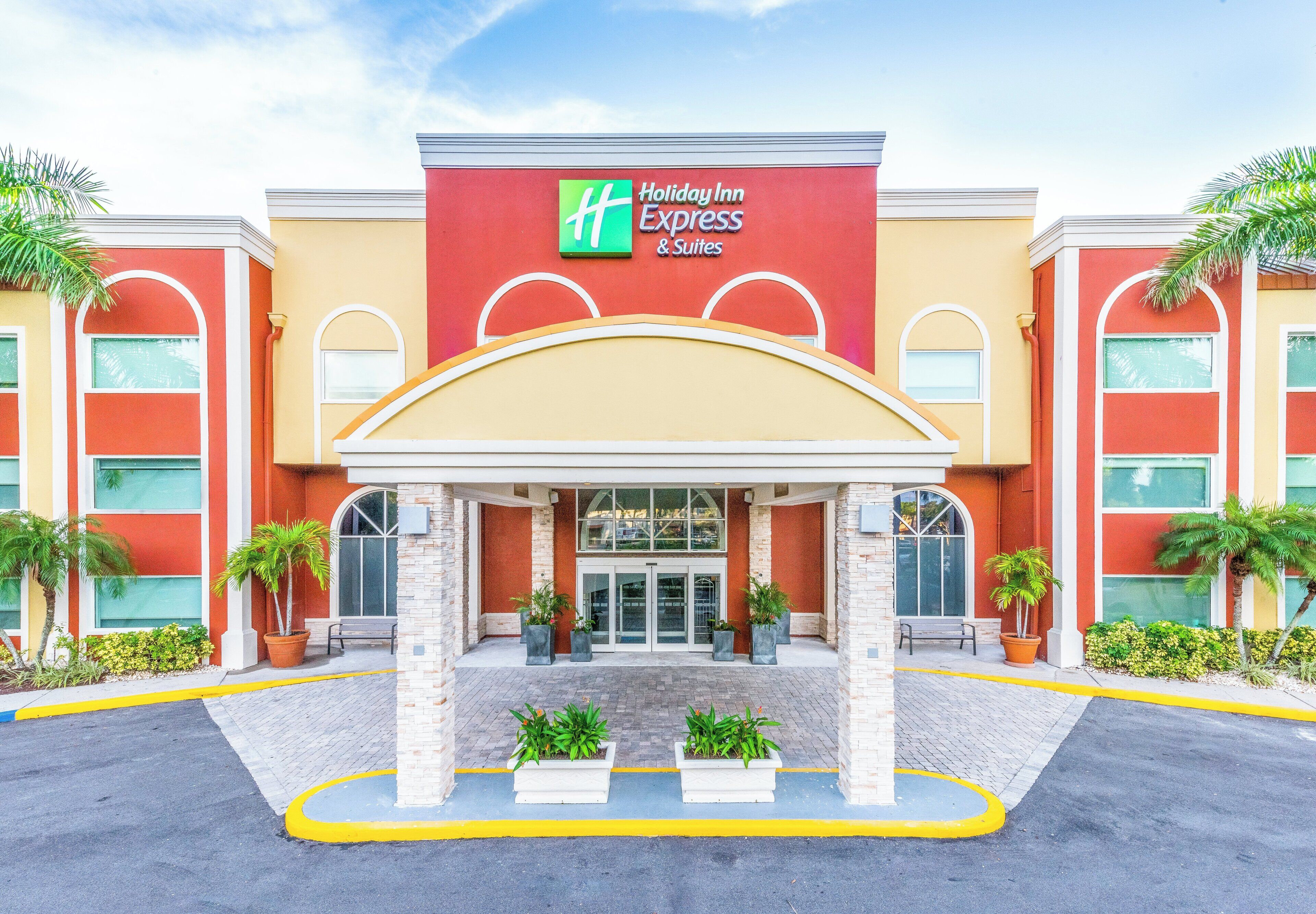 Edificio de Holiday Inn Express & Suites con fachada roja y color crema, entrada cubierta y plantas en macetas.