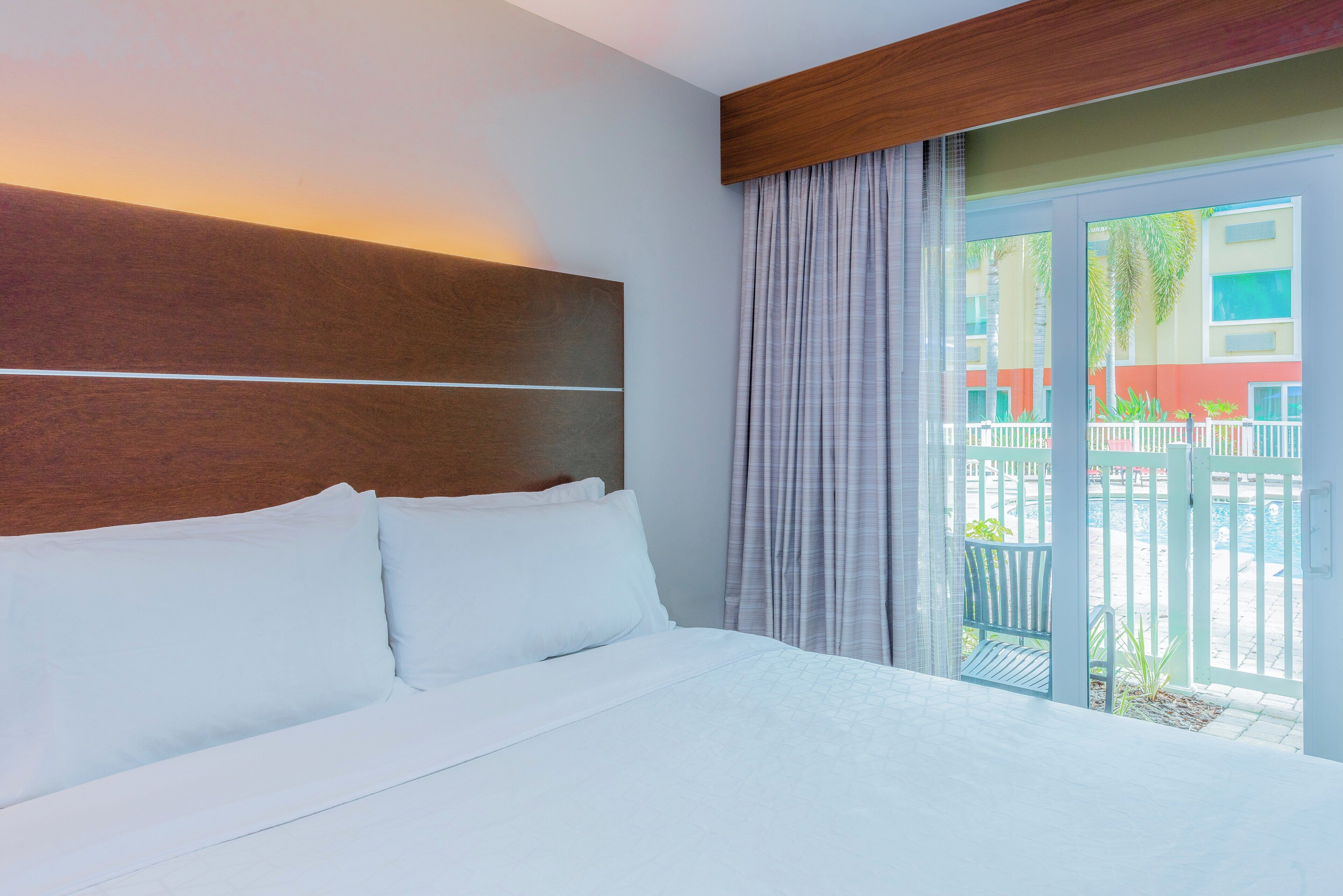 A hotel room with a bed, a wooden headboard, a view of the outside, and a balcony with a railing.