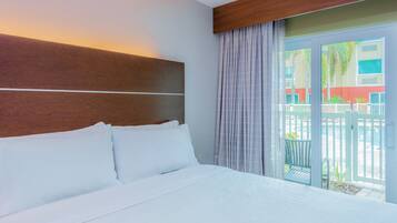 A hotel room with a bed, a wooden headboard, a view of the outside, and a balcony with a railing.