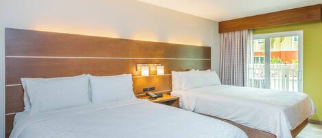 A hotel room with two beds, a wooden headboard, a nightstand with a phone, and a view of a balcony with a white fence.