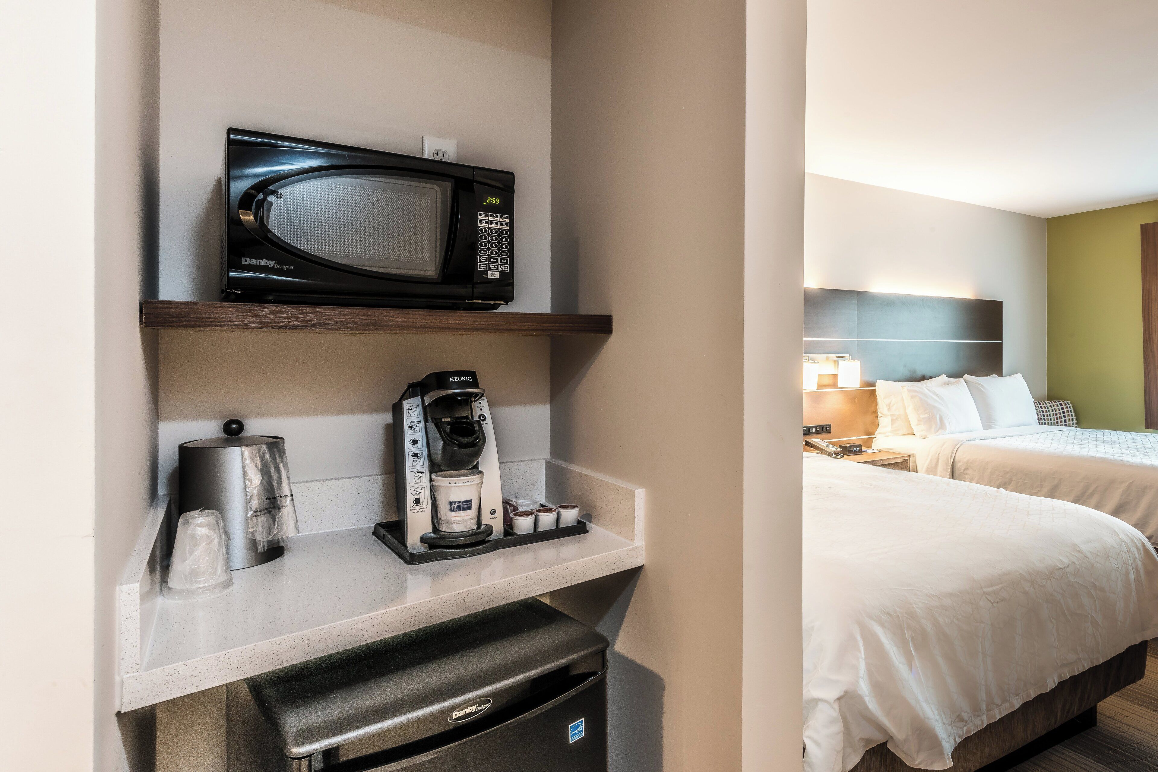 A hotel room with a microwave, coffee machine, and a small trash bin on a countertop.