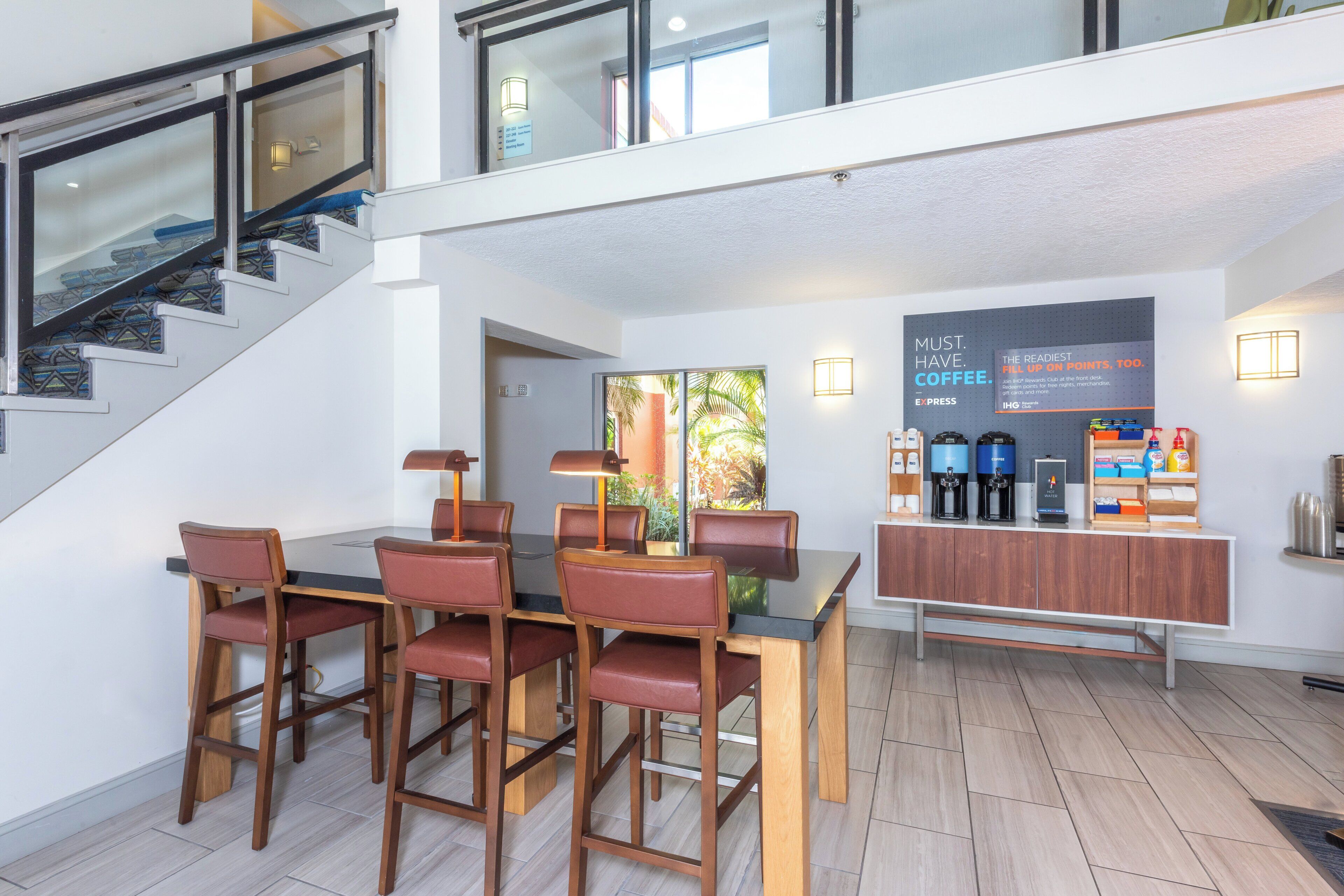 A modern hotel lobby with a dining area, a staircase, and a coffee station.