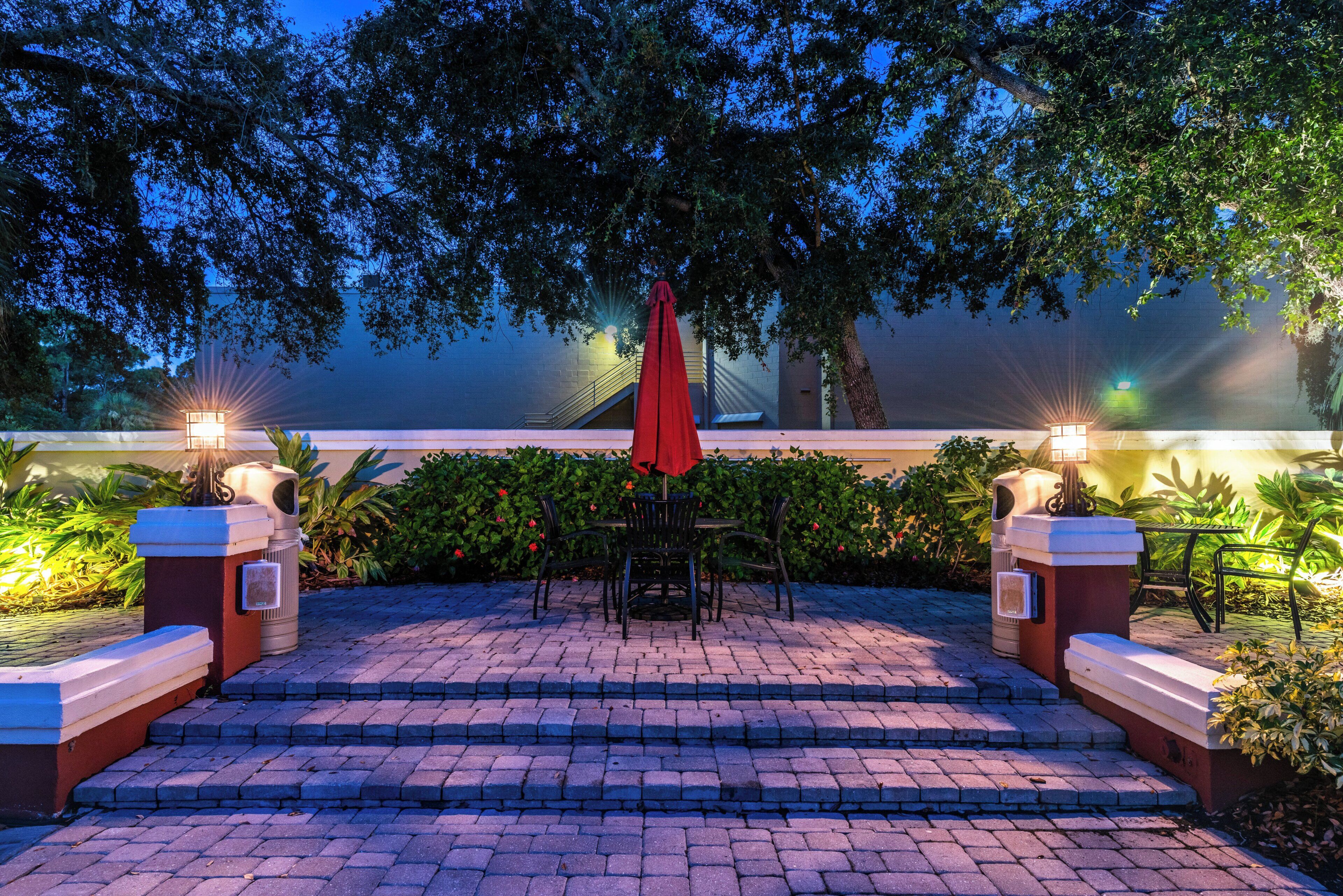 A patio with steps leading to a seating area, featuring a red umbrella and two wall-mounted lights.