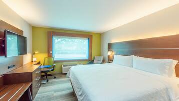 Una habitación de hotel con cama, escritorio, silla, televisor y ventana.