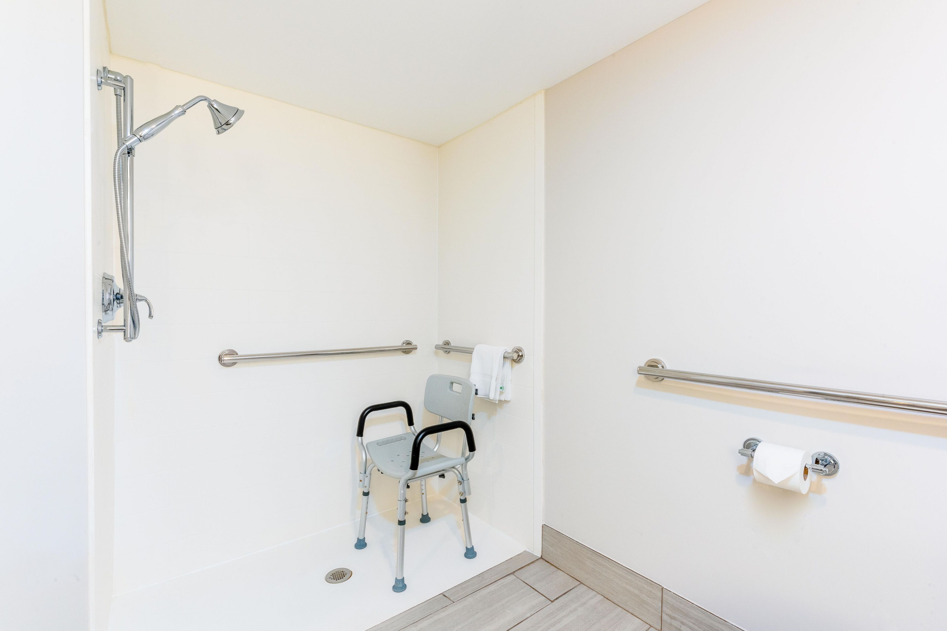 A bathroom with a wheelchair-accessible shower, grab bars, and a toilet paper holder.