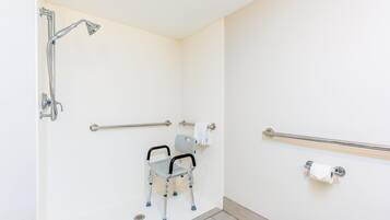 Casa de banho com chuveiro acessível para cadeiras de rodas, barras de apoio e suporte para papel higiénico.