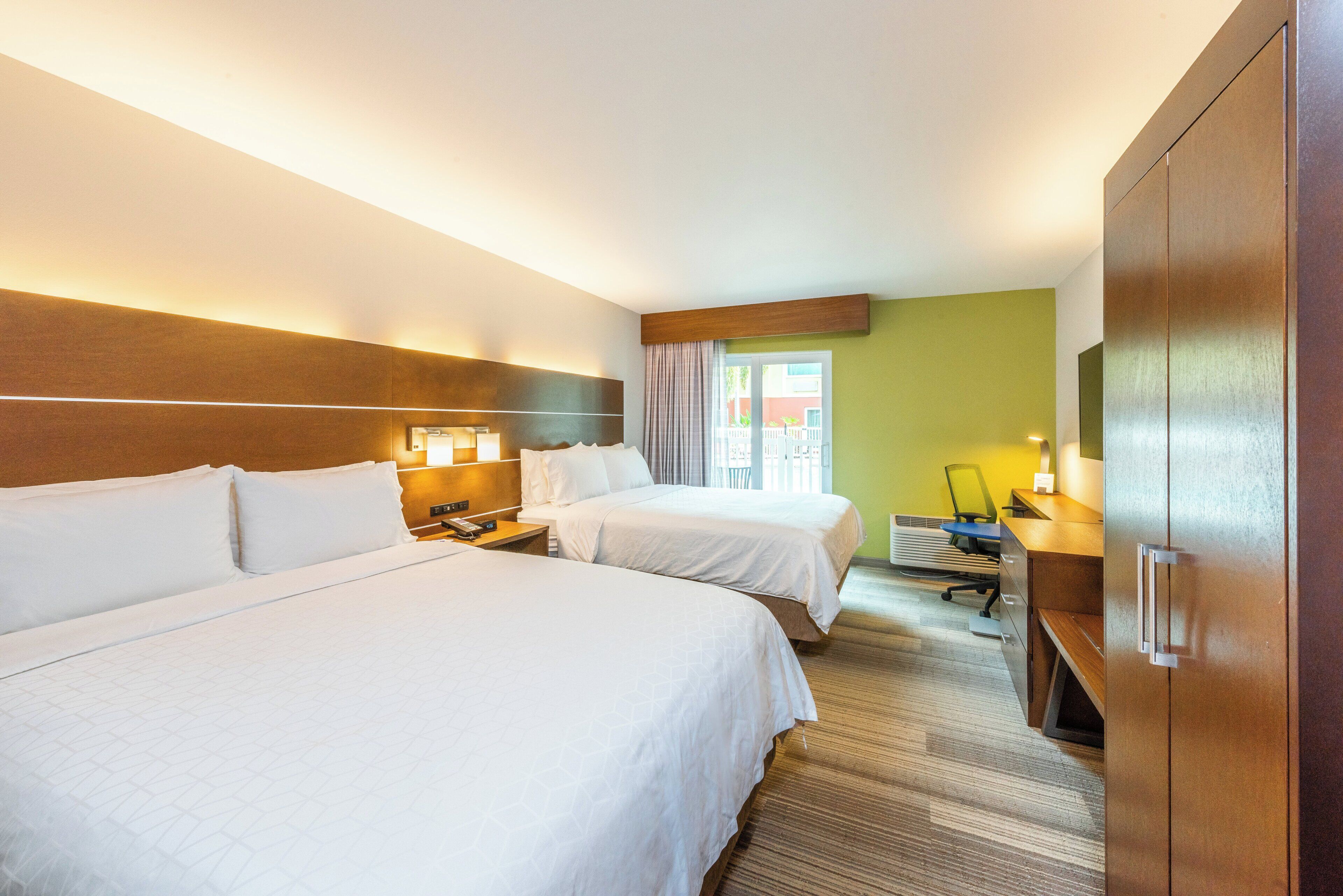 Habitación de hotel con dos camas, un escritorio, una silla, una lámpara y un armario.
