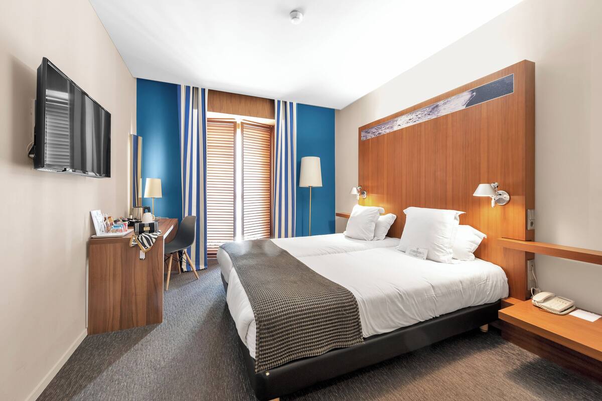 A hotel room with a large bed, a desk, a TV, and a wooden headboard.
