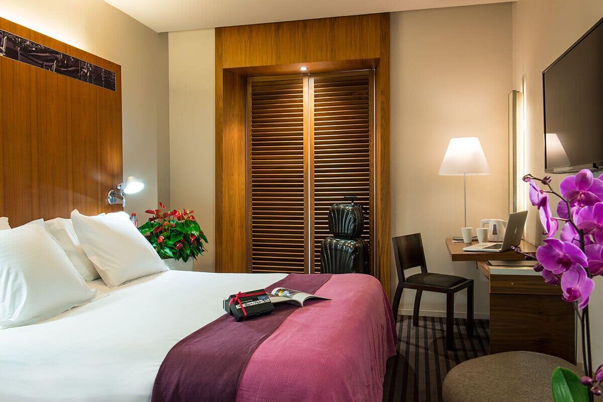 Ein Hotelzimmer mit Bett, Schreibtisch, Stuhl, Lampe und Kleiderschrank.