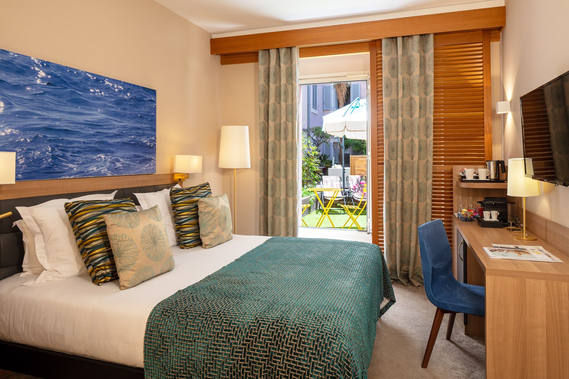 Habitación de hotel con cama, escritorio, silla, televisor y vistas al exterior.