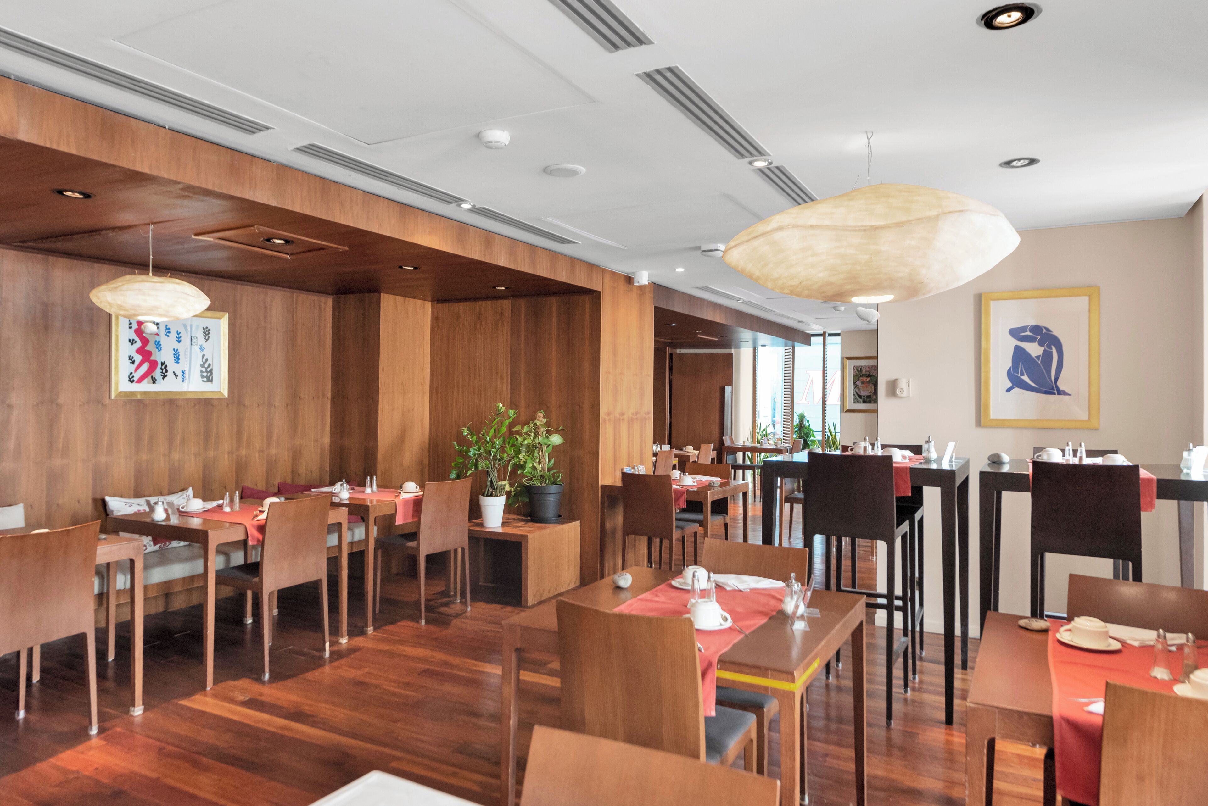 A restaurant with wooden paneling, multiple dining tables, chairs, and hanging pendant lights.