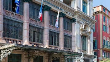 Een historisch gebouw met klassieke architectuur, voorzien van meerdere vlaggen, grote ramen en versierde balkons.